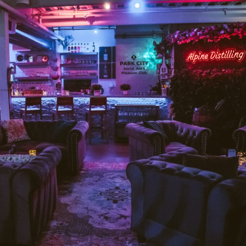 a darkly lit barroom with plush chairs and a glowing sign that says Alpine Distilling
