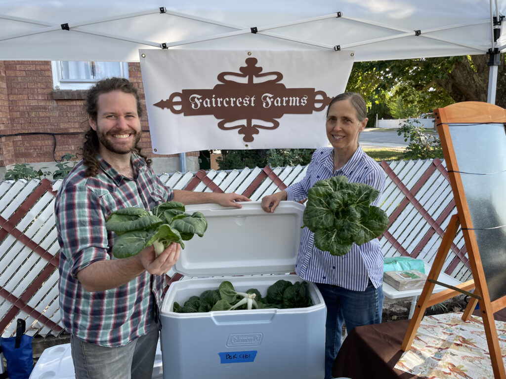 Two friends standing beside a vegetable-filled cooler at the farmers' market