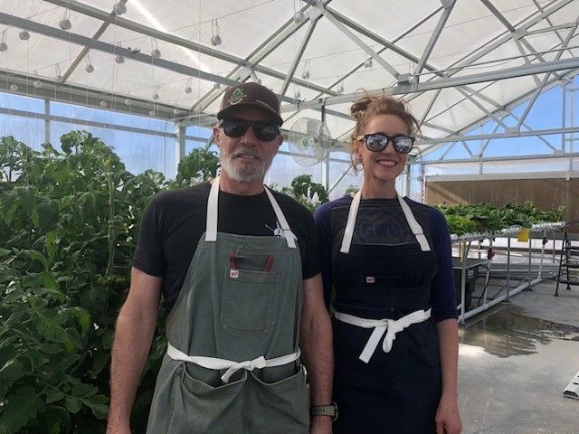 A man and a woman standing in a greenhouse surrounded by plants