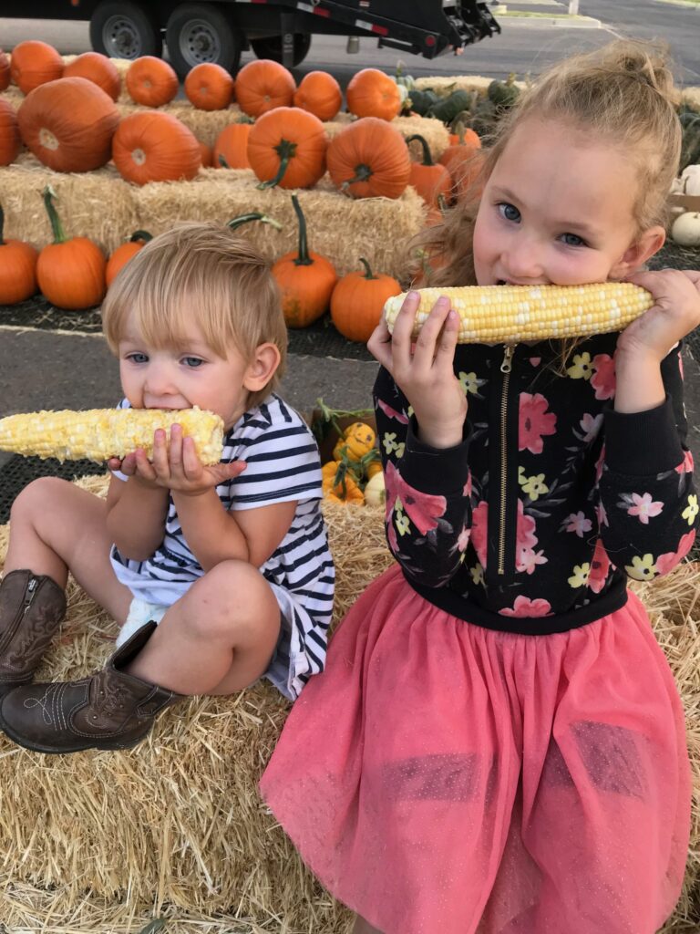 two kids enjoying corn on a hay bale