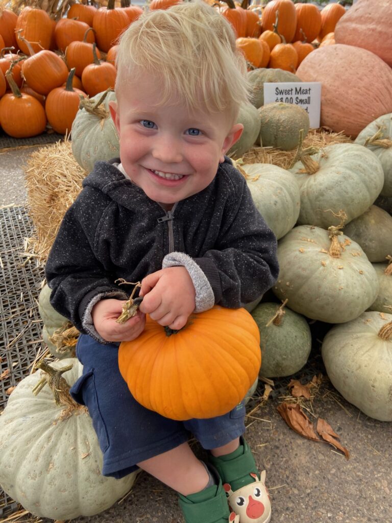 A young boy happily sitting on a pile of pumpkins