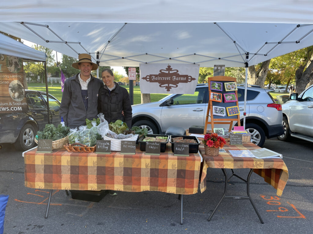 A couple browsing produce under a canopy at a farmers market