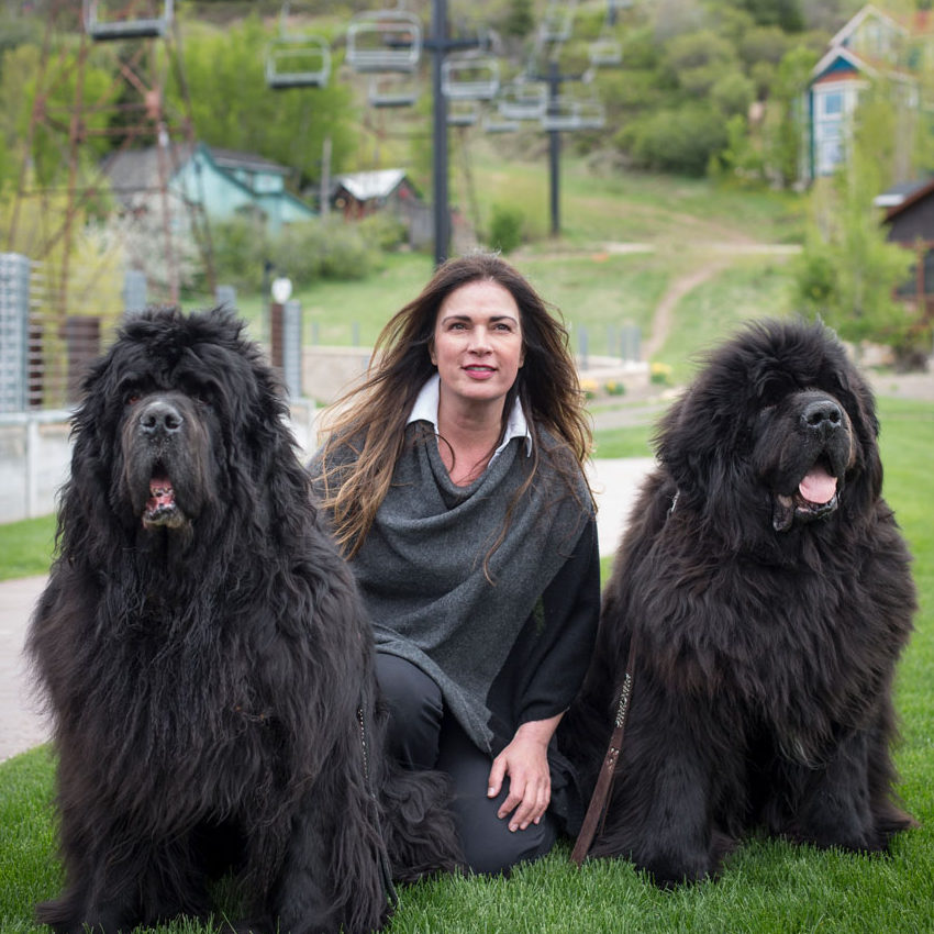 A woman relaxing in the grass with her three black dogs