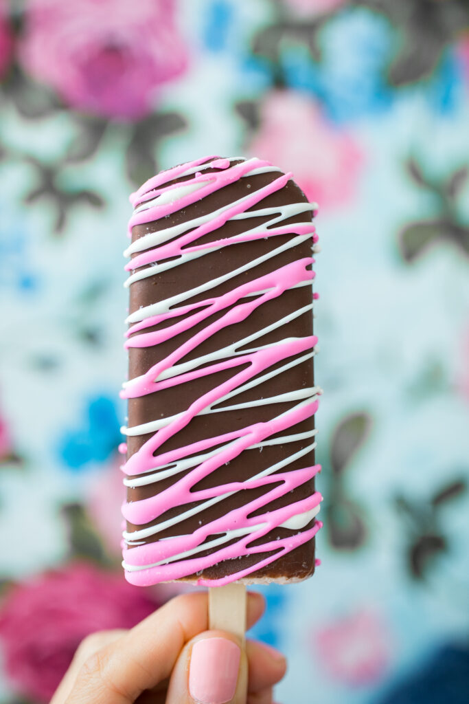 A hand holding a chocolate and pink striped ice cream cone