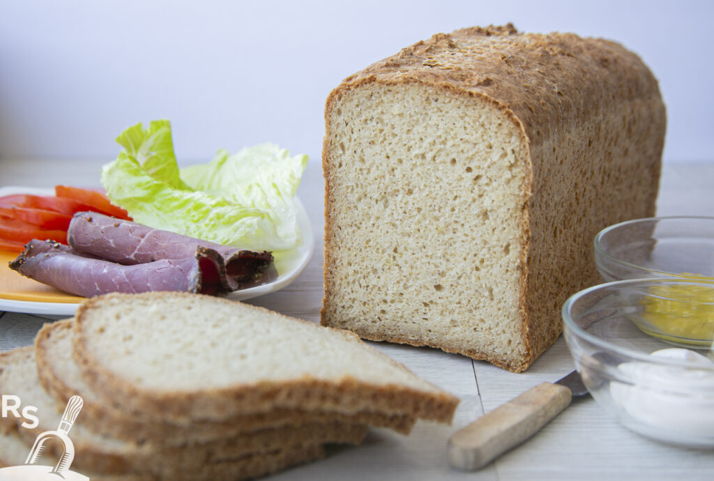 A loaf of bread displayed on a table beside a plate of food