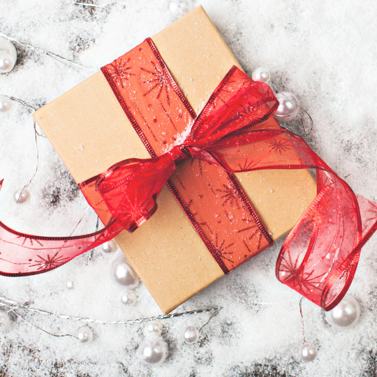 Image of a wrapped gift with brown paper and a red bow sitting on snow