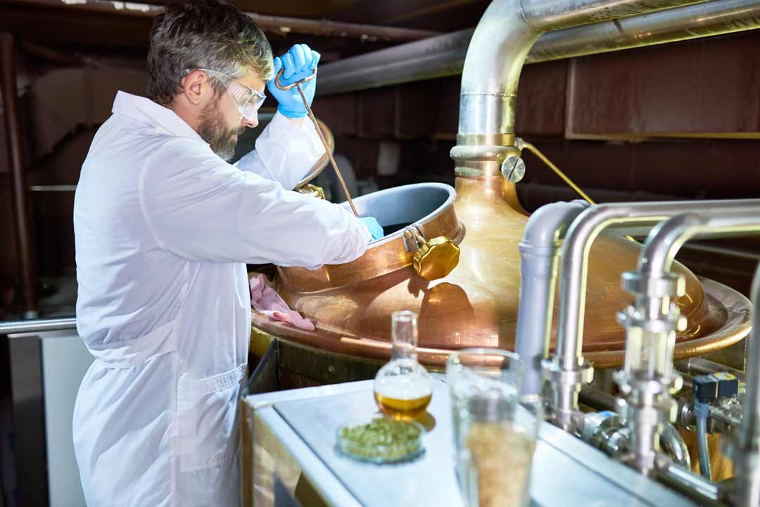 A scientist in a white lab coat pouring a glass of beer